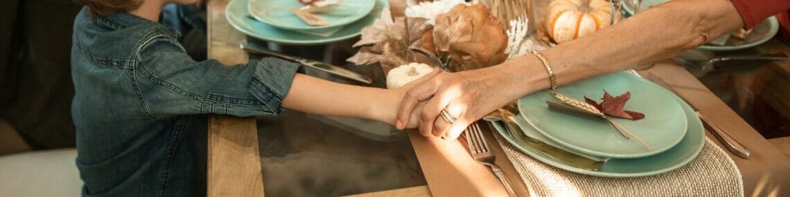a family holding their hands praying and sitting together on a dining table